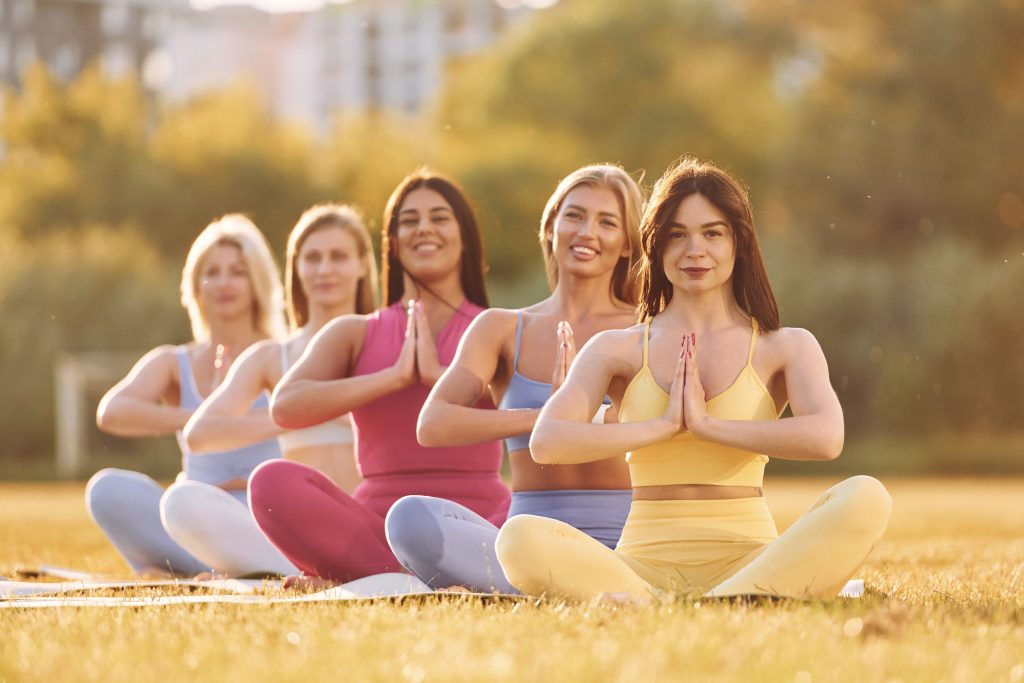 Calm meditation in lotus pose. Group of women have fitness outdoors on the field together.