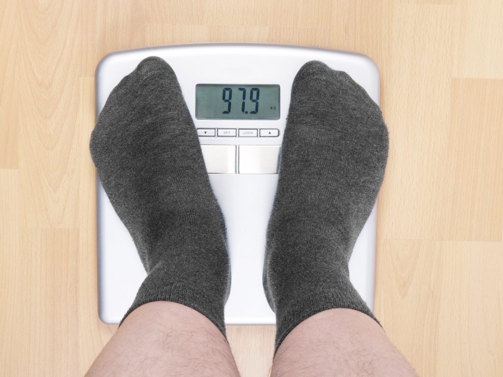 overweight man in socks standing on bathroom scales