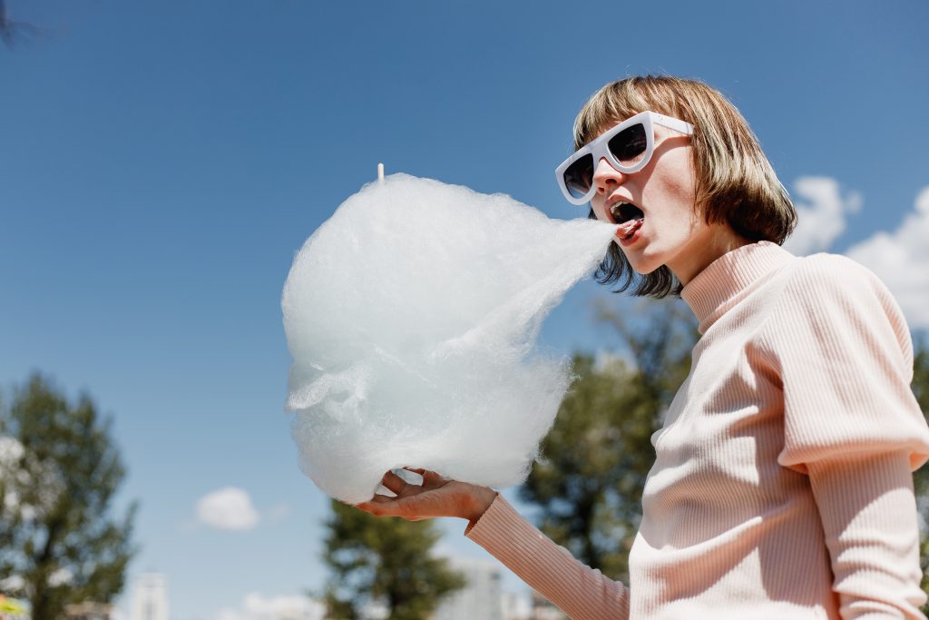 Stylish girl in a gently pink dress and white sunglasses eats a cotton candy in the street on a sunny day