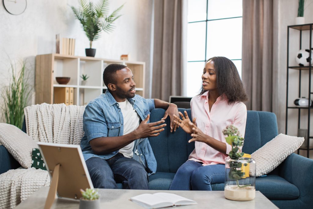 African american couple of young man and woman sitting together on comfy couch and chatting. Two loving people spending free time together at home.