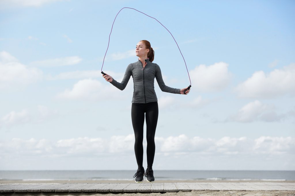 Healthy young woman with jump rope at the beach